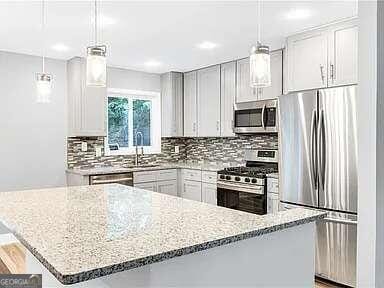 kitchen with stainless steel appliances, hanging light fixtures, light stone counters, and a breakfast bar area