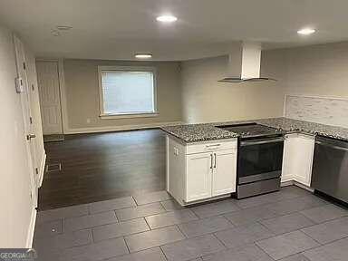 kitchen with wall chimney range hood, white cabinets, dark stone counters, dark hardwood / wood-style floors, and stainless steel appliances