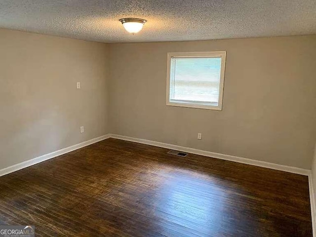 spare room with a textured ceiling and dark hardwood / wood-style flooring