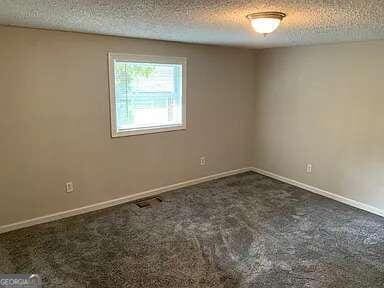 empty room featuring a textured ceiling and dark carpet