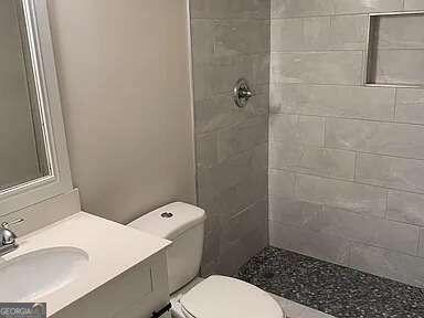 bathroom with toilet, vanity, and a tile shower