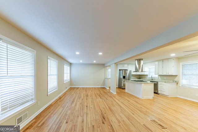 kitchen featuring wall chimney exhaust hood, light hardwood / wood-style flooring, stainless steel appliances, a wealth of natural light, and white cabinets