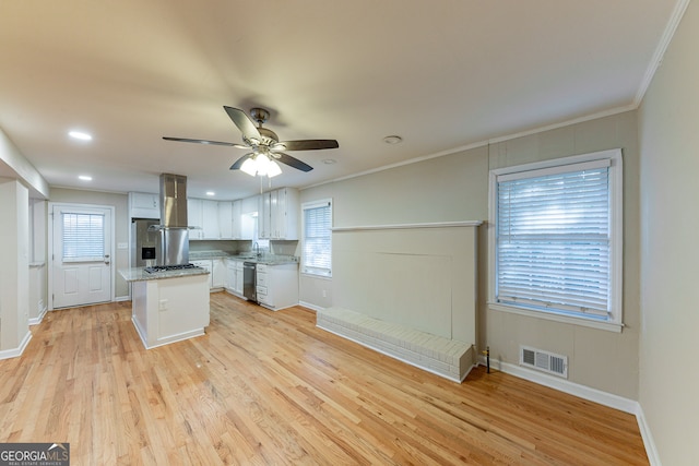 kitchen with a healthy amount of sunlight, wall chimney exhaust hood, a kitchen island, and white cabinets