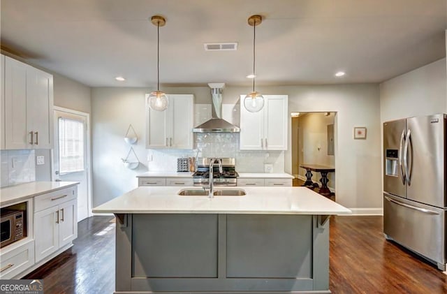 kitchen with appliances with stainless steel finishes, wall chimney exhaust hood, white cabinets, and hanging light fixtures