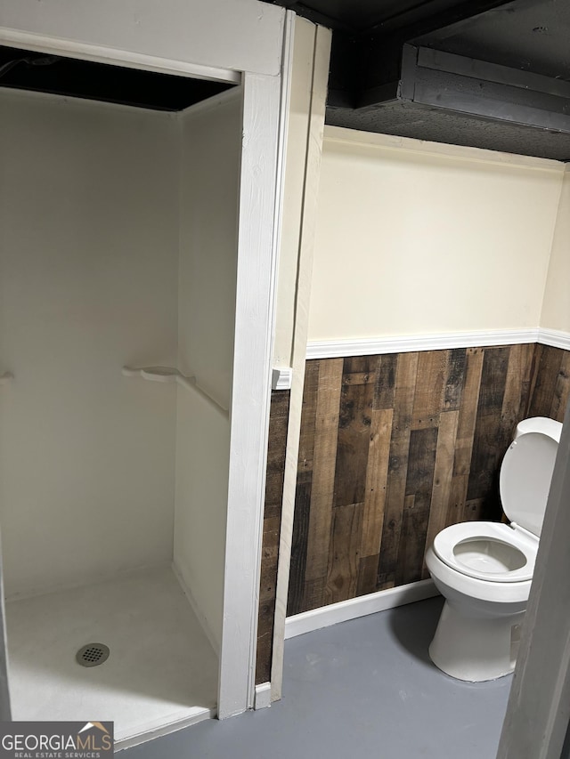 bathroom with toilet, wooden walls, and concrete flooring