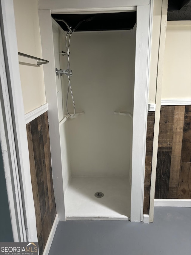 bathroom featuring wood walls, concrete flooring, and walk in shower