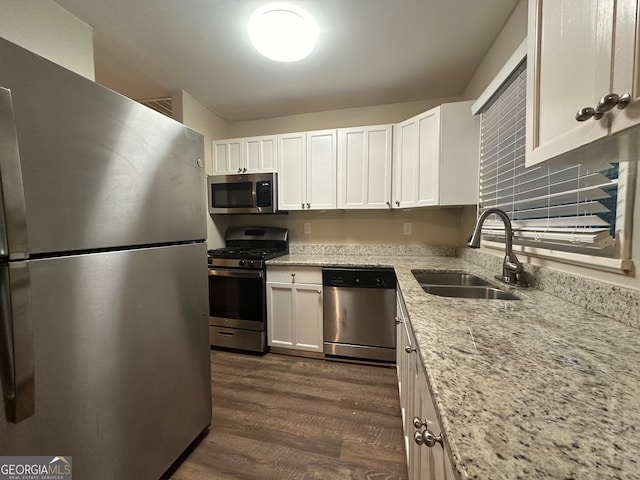 kitchen featuring appliances with stainless steel finishes, sink, white cabinets, dark wood-type flooring, and light stone counters