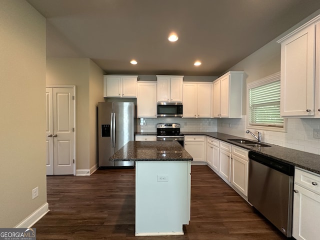 kitchen featuring a kitchen island, dark hardwood / wood-style floors, stainless steel appliances, dark stone counters, and sink