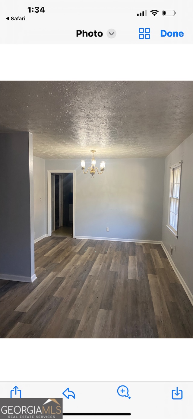 empty room featuring dark wood-type flooring, a textured ceiling, and a chandelier