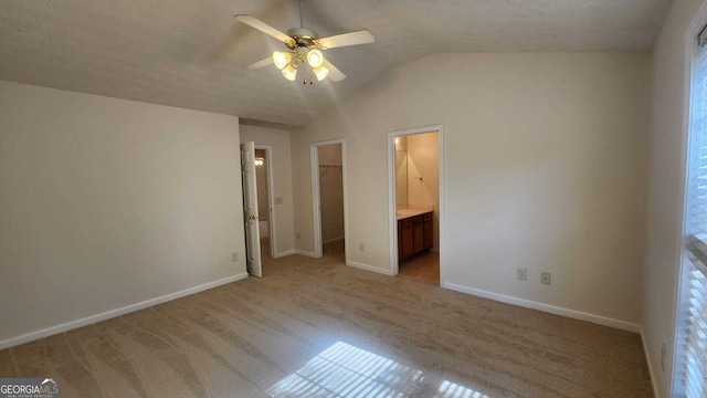 unfurnished bedroom featuring a walk in closet, light carpet, ceiling fan, lofted ceiling, and connected bathroom