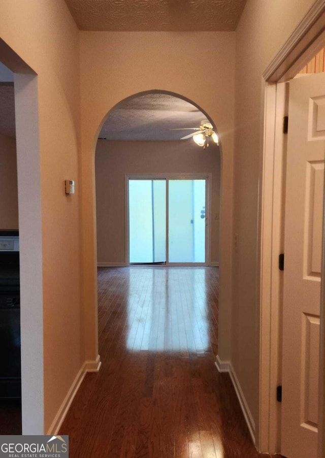 corridor with a textured ceiling and dark hardwood / wood-style flooring