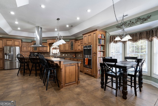 kitchen featuring appliances with stainless steel finishes, a kitchen island with sink, island range hood, and pendant lighting