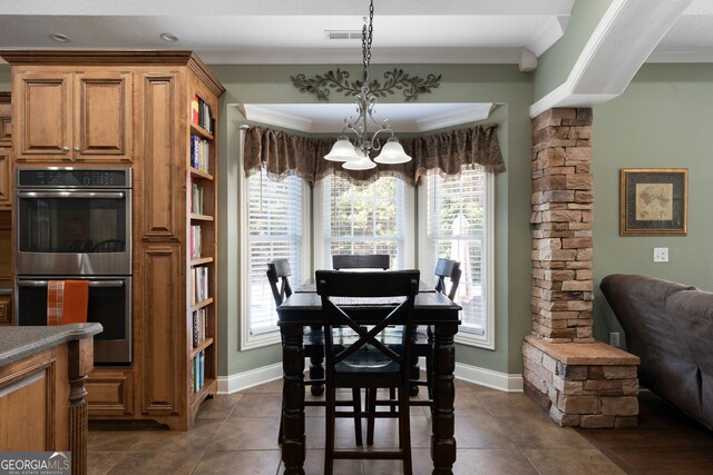 dining area with dark tile patterned flooring, crown molding, a chandelier, and ornate columns