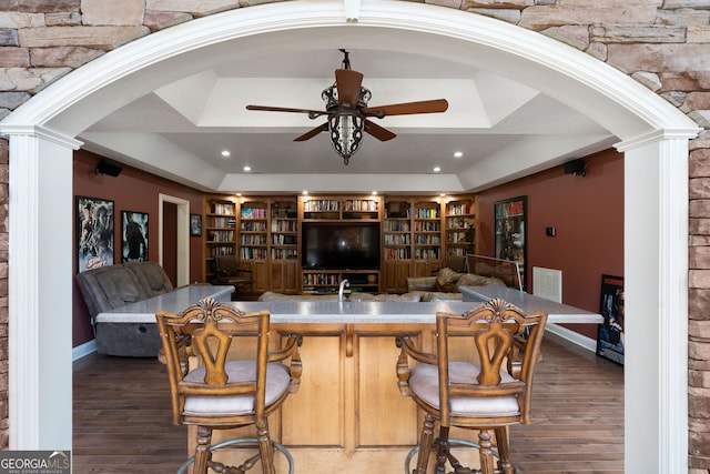 bar with ceiling fan, ornate columns, a tray ceiling, and dark hardwood / wood-style flooring