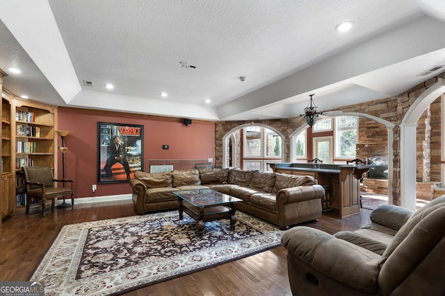 living room featuring dark wood-type flooring, a textured ceiling, and decorative columns