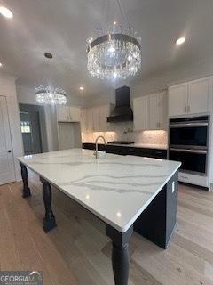 kitchen with decorative light fixtures, a large island, custom range hood, appliances with stainless steel finishes, and white cabinetry