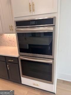 interior details featuring stainless steel double oven, light countertops, light wood finished floors, and white cabinetry