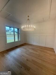 unfurnished dining area with a chandelier, a decorative wall, and wood finished floors