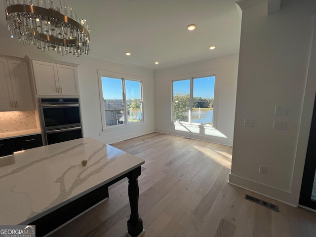 kitchen with double oven, light stone counters, visible vents, light wood-style floors, and white cabinets