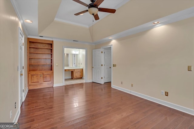 unfurnished bedroom with connected bathroom, built in desk, wood-type flooring, ornamental molding, and ceiling fan