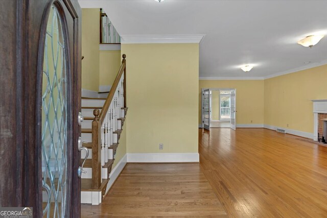 foyer entrance featuring crown molding, light wood-type flooring, and a fireplace