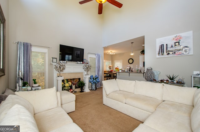 carpeted living room featuring a fireplace, a high ceiling, and ceiling fan