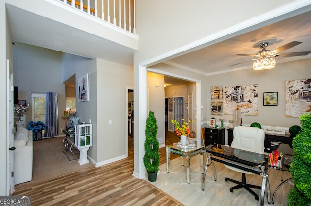 home office featuring ornamental molding, wood-type flooring, a towering ceiling, and ceiling fan