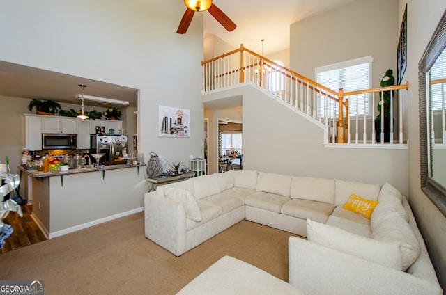 carpeted living room with a towering ceiling, ceiling fan with notable chandelier, and a wealth of natural light