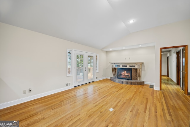 unfurnished living room with french doors, lofted ceiling, light hardwood / wood-style flooring, and a brick fireplace