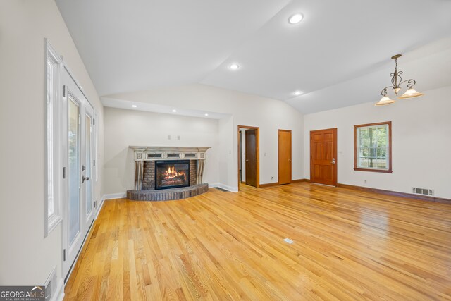 unfurnished living room featuring light hardwood / wood-style floors, lofted ceiling, a brick fireplace, and an inviting chandelier