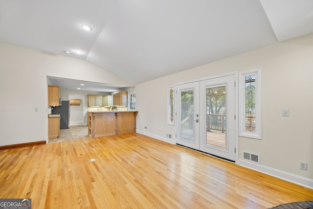 unfurnished living room with lofted ceiling, french doors, and light wood-type flooring