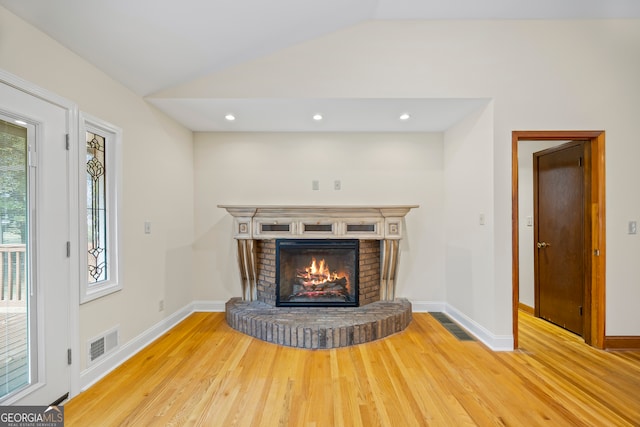 unfurnished living room featuring lofted ceiling, a brick fireplace, and hardwood / wood-style flooring