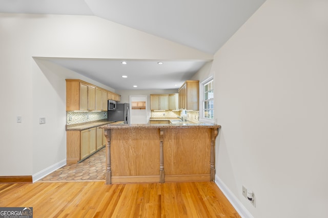 kitchen featuring kitchen peninsula, decorative backsplash, light brown cabinetry, vaulted ceiling, and light hardwood / wood-style flooring