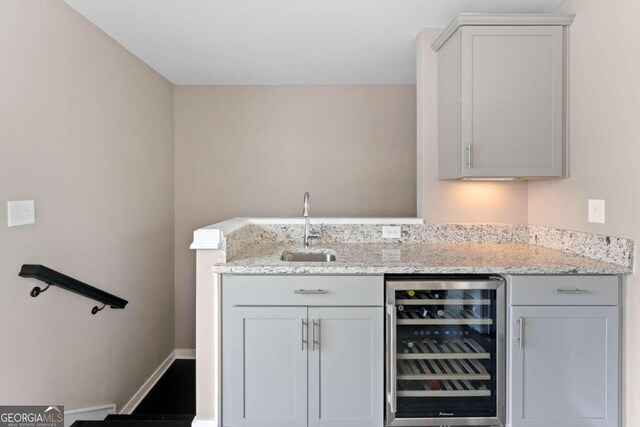 bar with wine cooler, light stone countertops, and sink