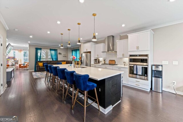 kitchen featuring wall chimney range hood, a large island, decorative light fixtures, white cabinetry, and appliances with stainless steel finishes