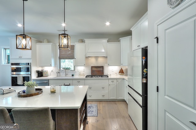 kitchen with light wood-type flooring, stainless steel appliances, pendant lighting, white cabinets, and premium range hood