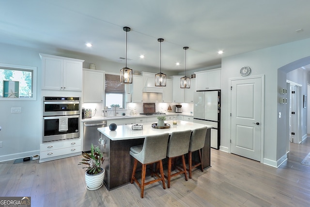 kitchen with white cabinets, hanging light fixtures, a kitchen island, appliances with stainless steel finishes, and light hardwood / wood-style floors