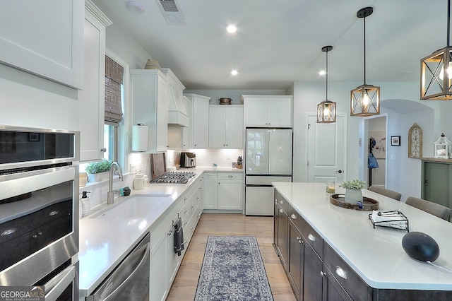 kitchen with appliances with stainless steel finishes, white cabinetry, sink, and hanging light fixtures