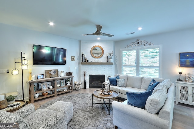 living room with ceiling fan, wood-type flooring, and a brick fireplace