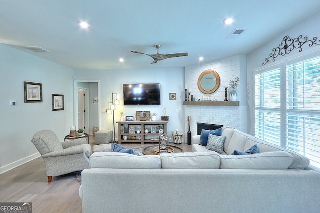 living room featuring ceiling fan, wood-type flooring, and a brick fireplace