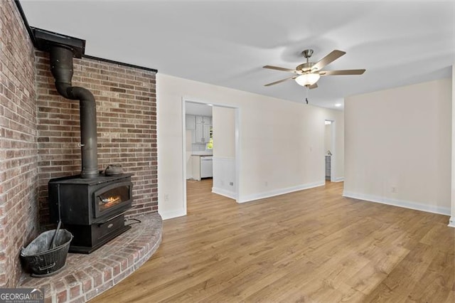 living room featuring light hardwood / wood-style flooring, brick wall, a wood stove, and ceiling fan