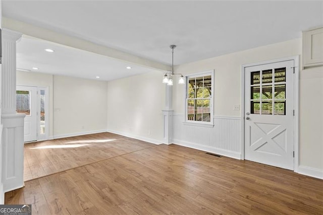 unfurnished dining area featuring a chandelier, ornate columns, and hardwood / wood-style flooring