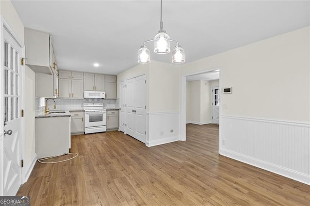 kitchen featuring white appliances, sink, light wood-type flooring, hanging light fixtures, and decorative backsplash