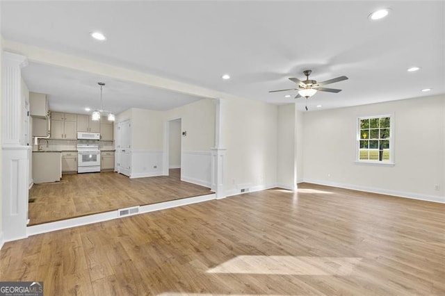 unfurnished living room with decorative columns, light wood-type flooring, and ceiling fan