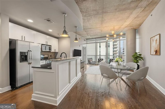 kitchen with appliances with stainless steel finishes, backsplash, dark hardwood / wood-style flooring, hanging light fixtures, and white cabinetry