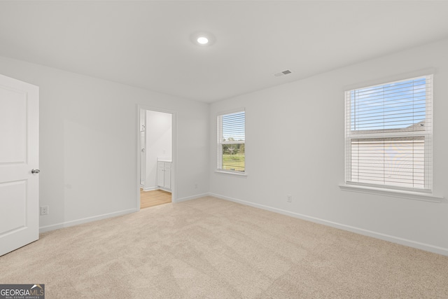 unfurnished bedroom featuring light carpet and ensuite bathroom