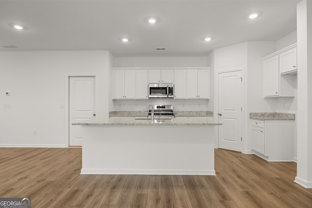 kitchen with appliances with stainless steel finishes, white cabinets, a kitchen island with sink, and light hardwood / wood-style floors