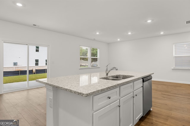 kitchen with a kitchen island with sink, sink, light wood-type flooring, stainless steel dishwasher, and white cabinetry