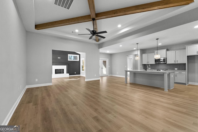 unfurnished living room featuring sink, ceiling fan, a fireplace, beamed ceiling, and light hardwood / wood-style floors