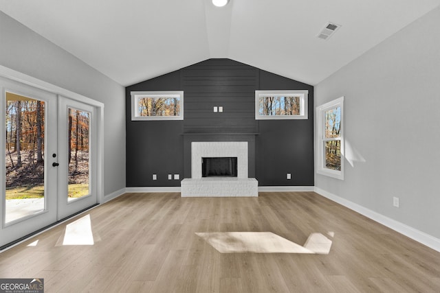 unfurnished living room with plenty of natural light, lofted ceiling, french doors, and a brick fireplace